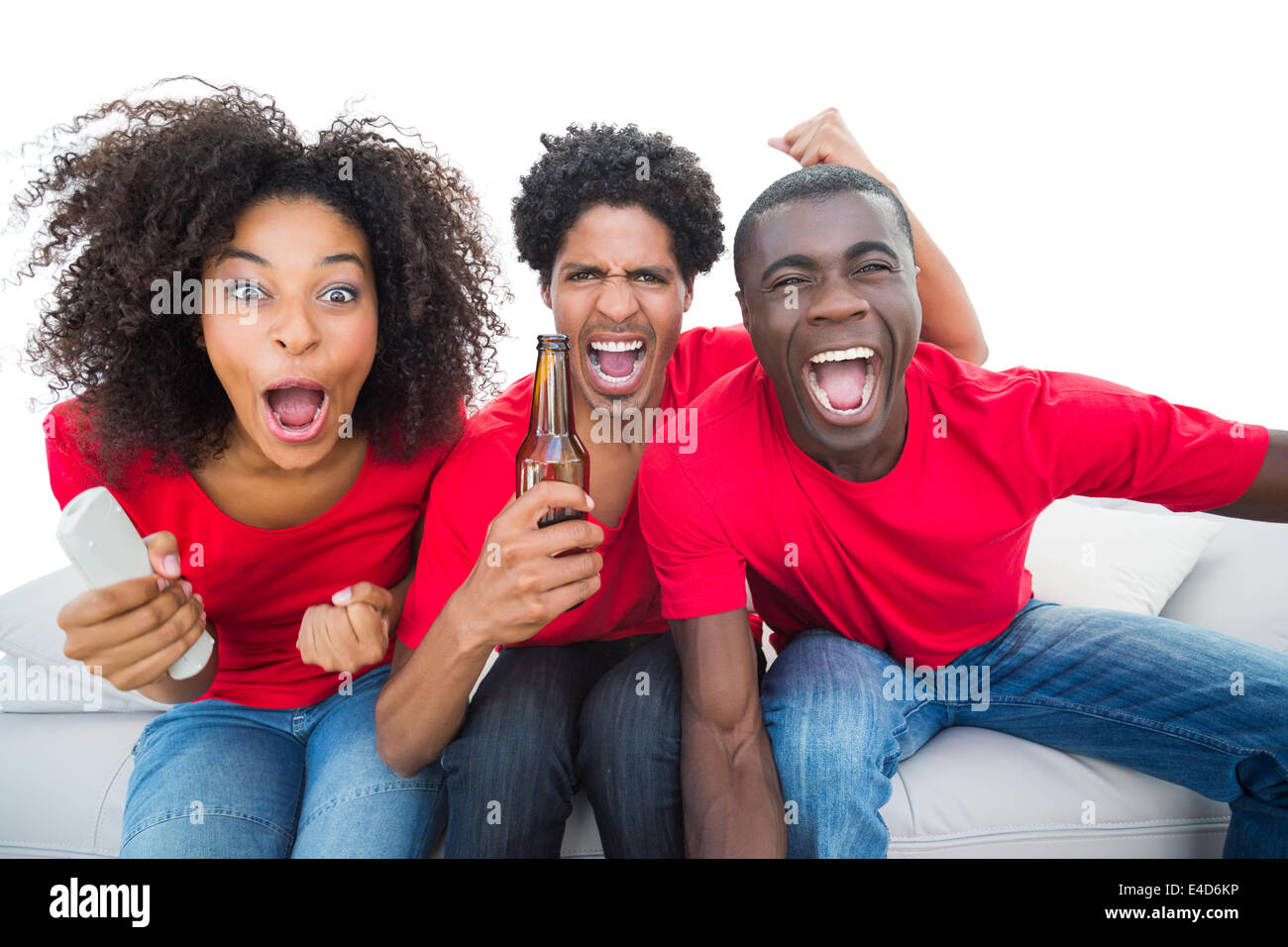 Football fans in red cheering on the sofa with beers Stock Photo