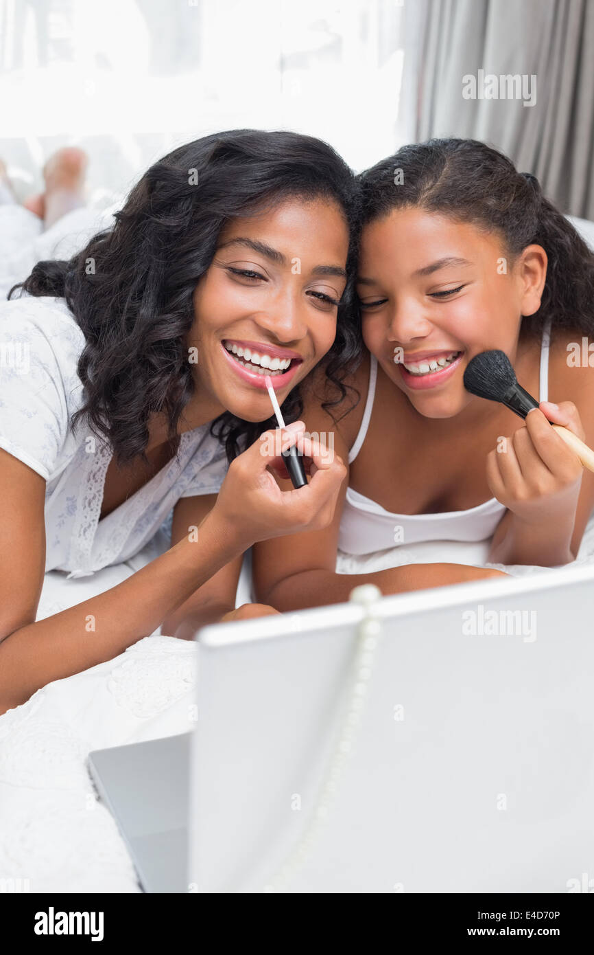 Smiling mother and daughter using laptop together on bed putting on