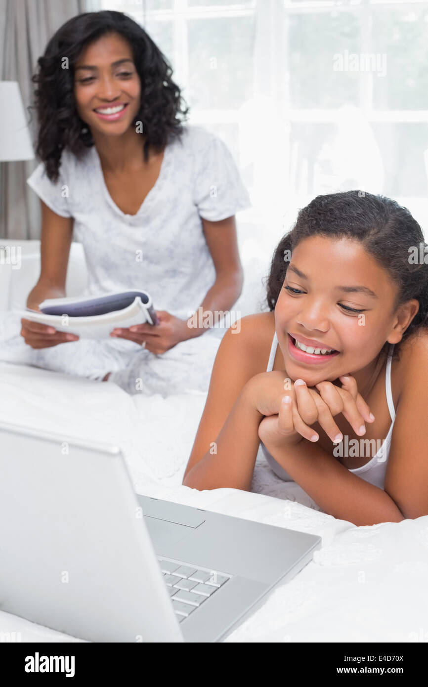 Mother reading magazine with daughter using laptop on bed Stock Photo