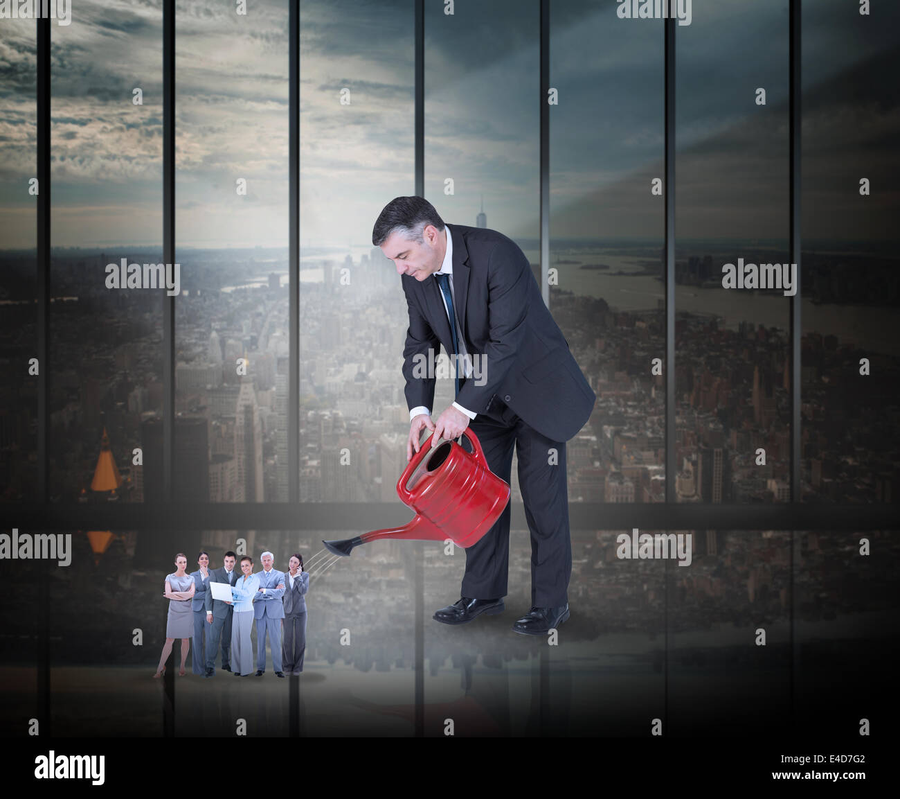 Composite image of mature businessman watering tiny business team Stock Photo