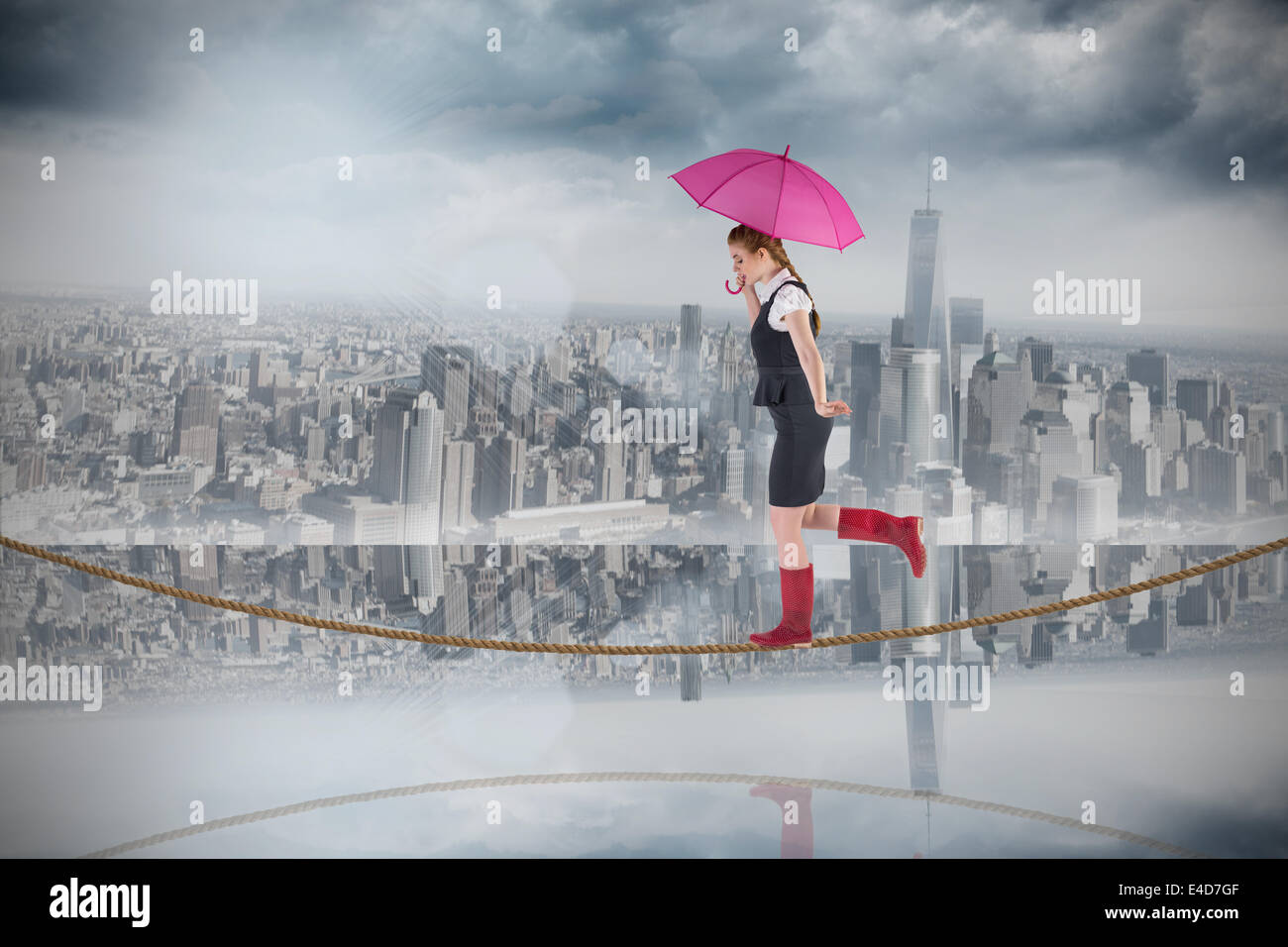 Composite image of pretty redhead businesswoman holding umbrella on tightrope Stock Photo