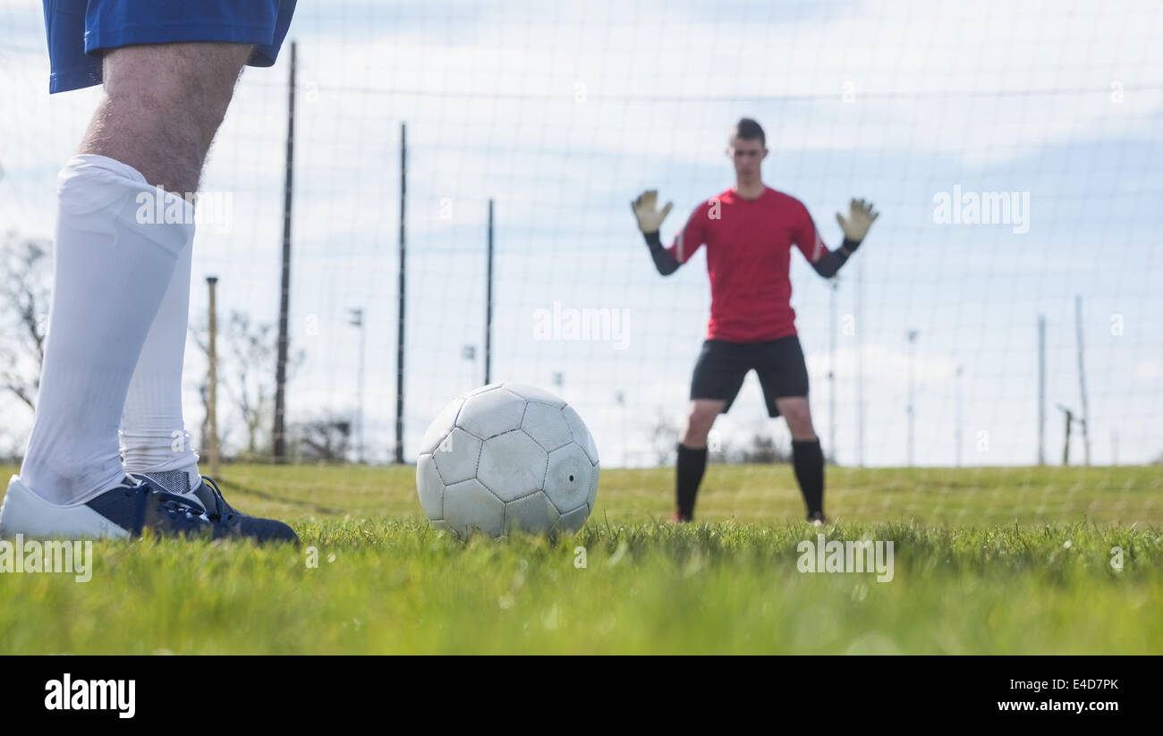 Goalkeeper in red waiting for striker to hit ball Stock Photo