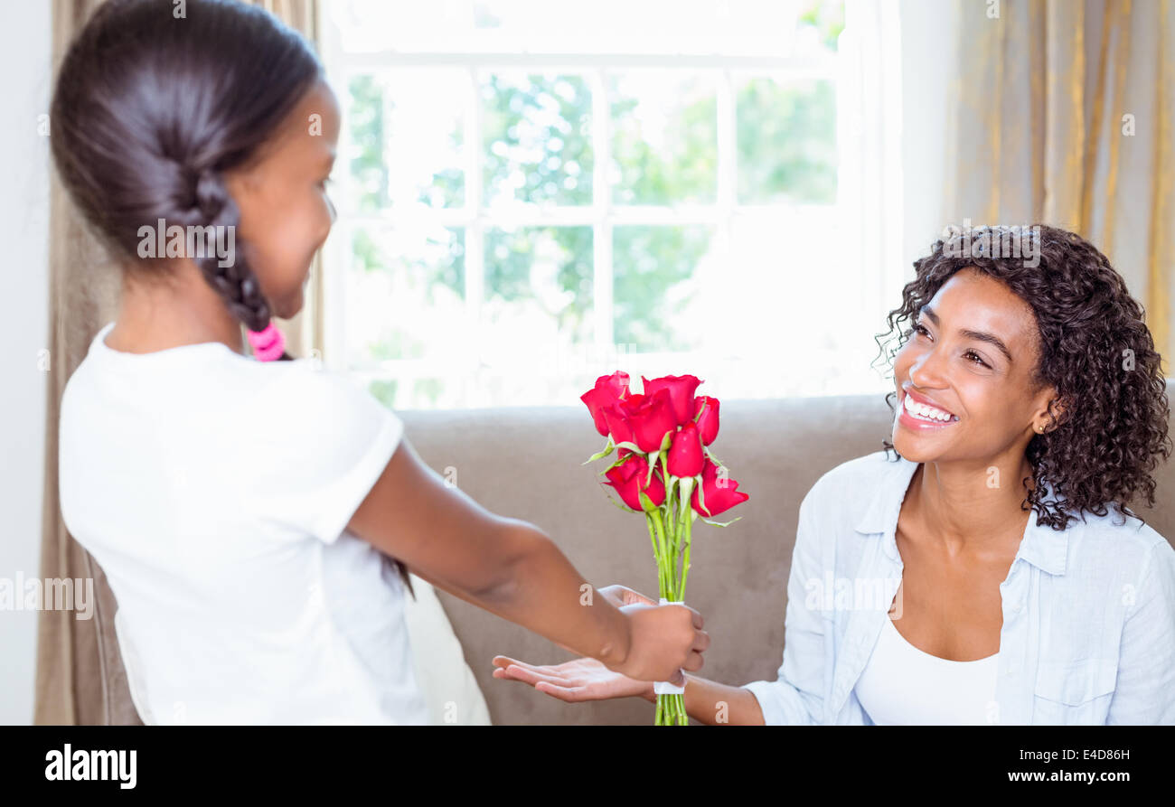 Pretty mother sitting on the couch with her daughter offering roses ...