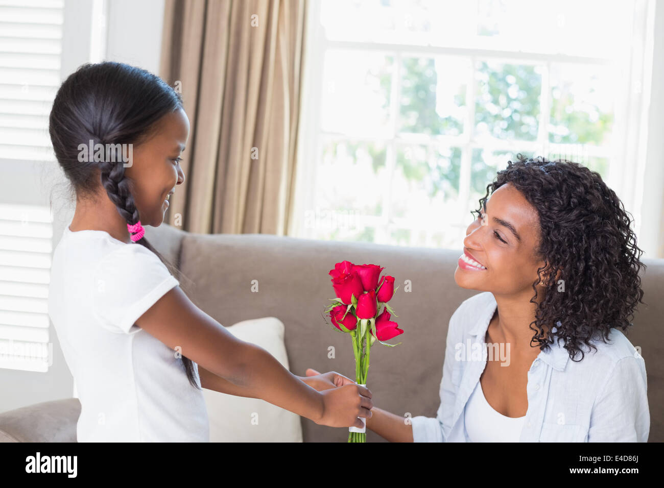 Pretty mother sitting on the couch with her daughter offering roses ...