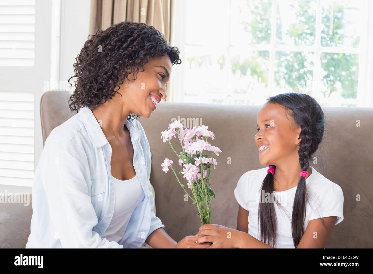 Pretty mother sitting on the couch with her daughter offering flowers Stock Photo