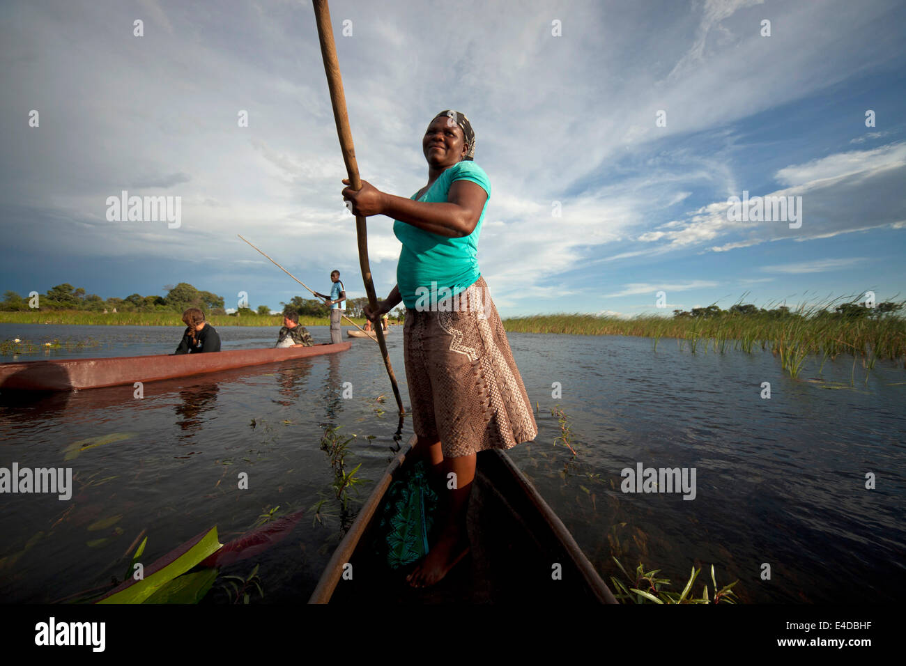 Frau mit typischer Stake oder Stange auf einem traditionellem Mokoro Boot und Touristen im Okavango Delta, Botswana, Afrika  | f Stock Photo