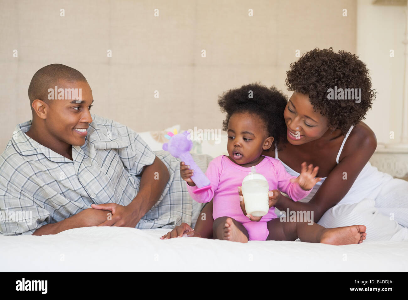 Happy parents and baby girl sitting on bed together Stock Photo