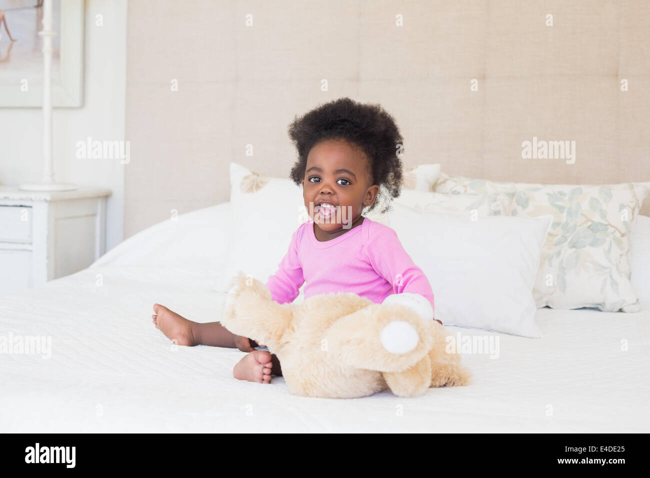 Baby girl in pink babygro sitting on bed Stock Photo
