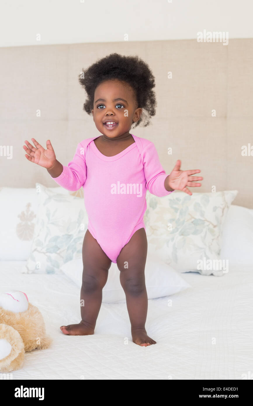 Baby girl in pink babygro standing on bed Stock Photo