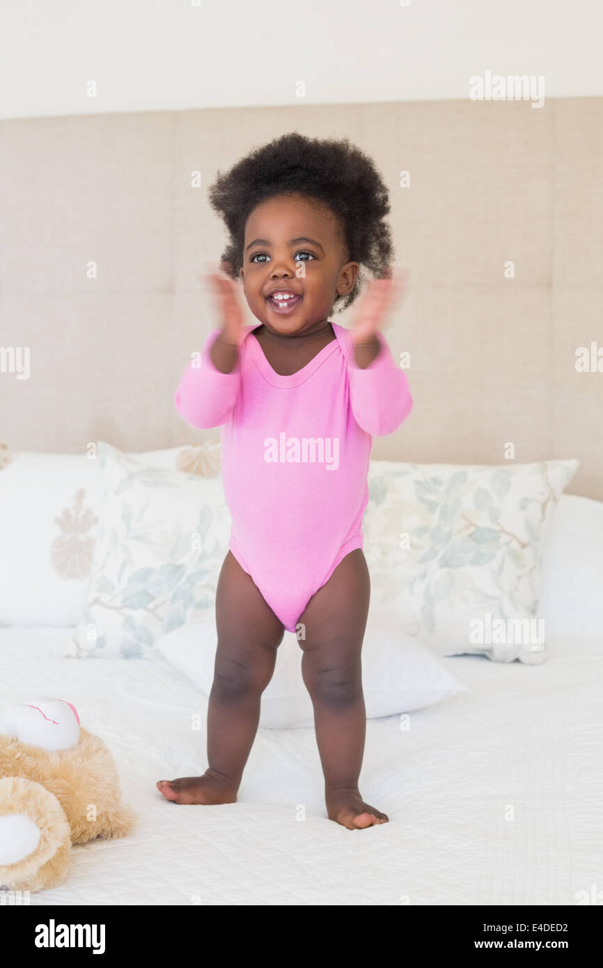 Baby girl in pink babygro standing on bed Stock Photo