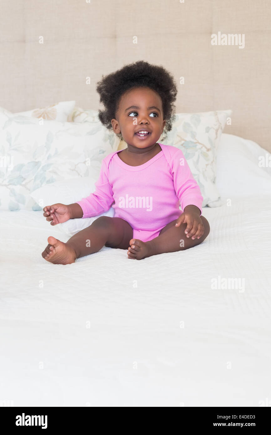 Baby girl in pink babygro sitting on bed Stock Photo