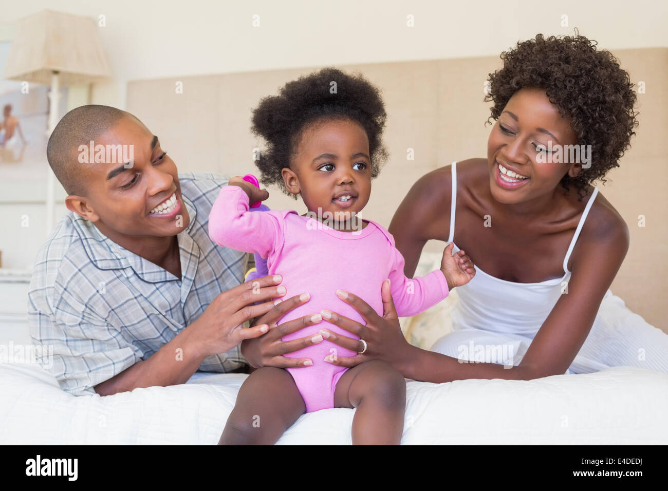 Happy parents playing with baby girl on bed together Stock Photo