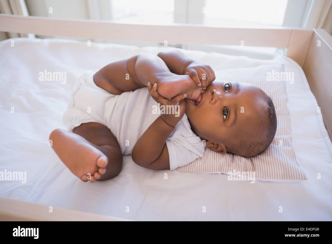 Adorable baby boy lying in his crib chewing foot Stock Photo