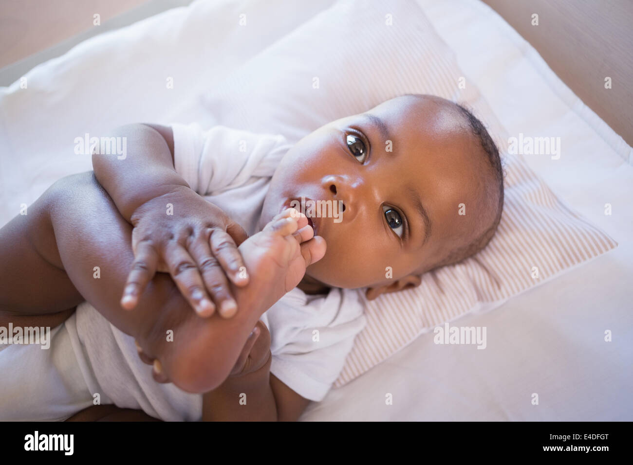 Adorable baby boy lying in his crib holding foot Stock Photo