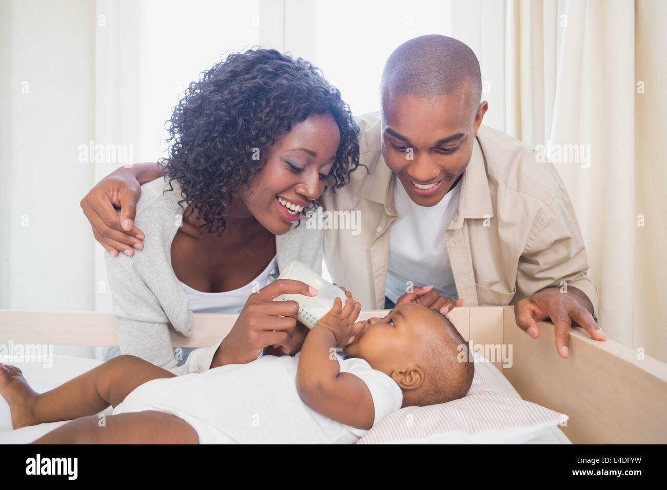 Happy parents feeding their baby boy in his crib Stock Photo