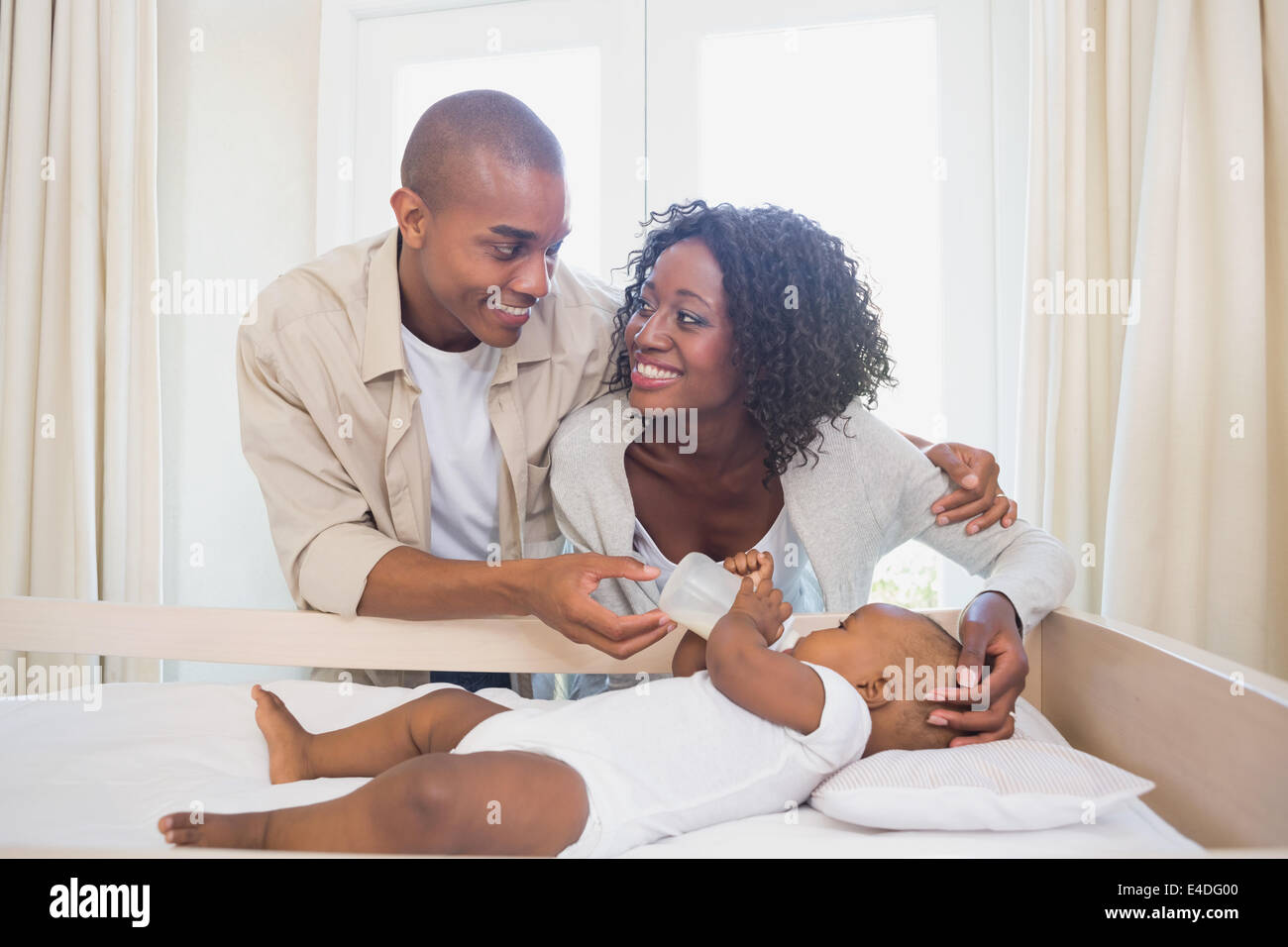 Happy parents feeding their baby boy in his crib Stock Photo