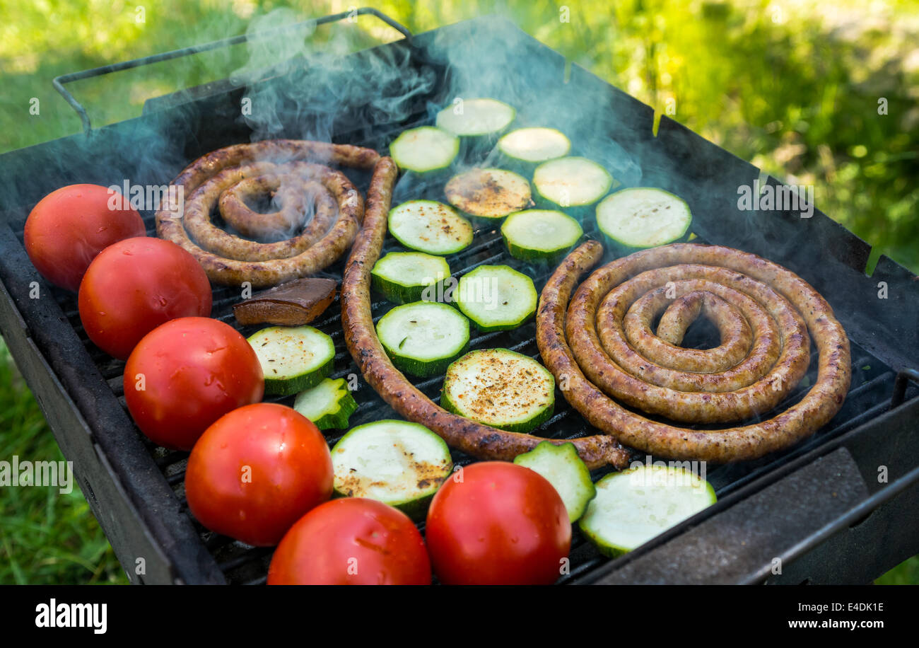 Mixed smoked barbecue with tomatoes cucurbita pepo eggplant and sausage on outdoor green background. Stock Photo