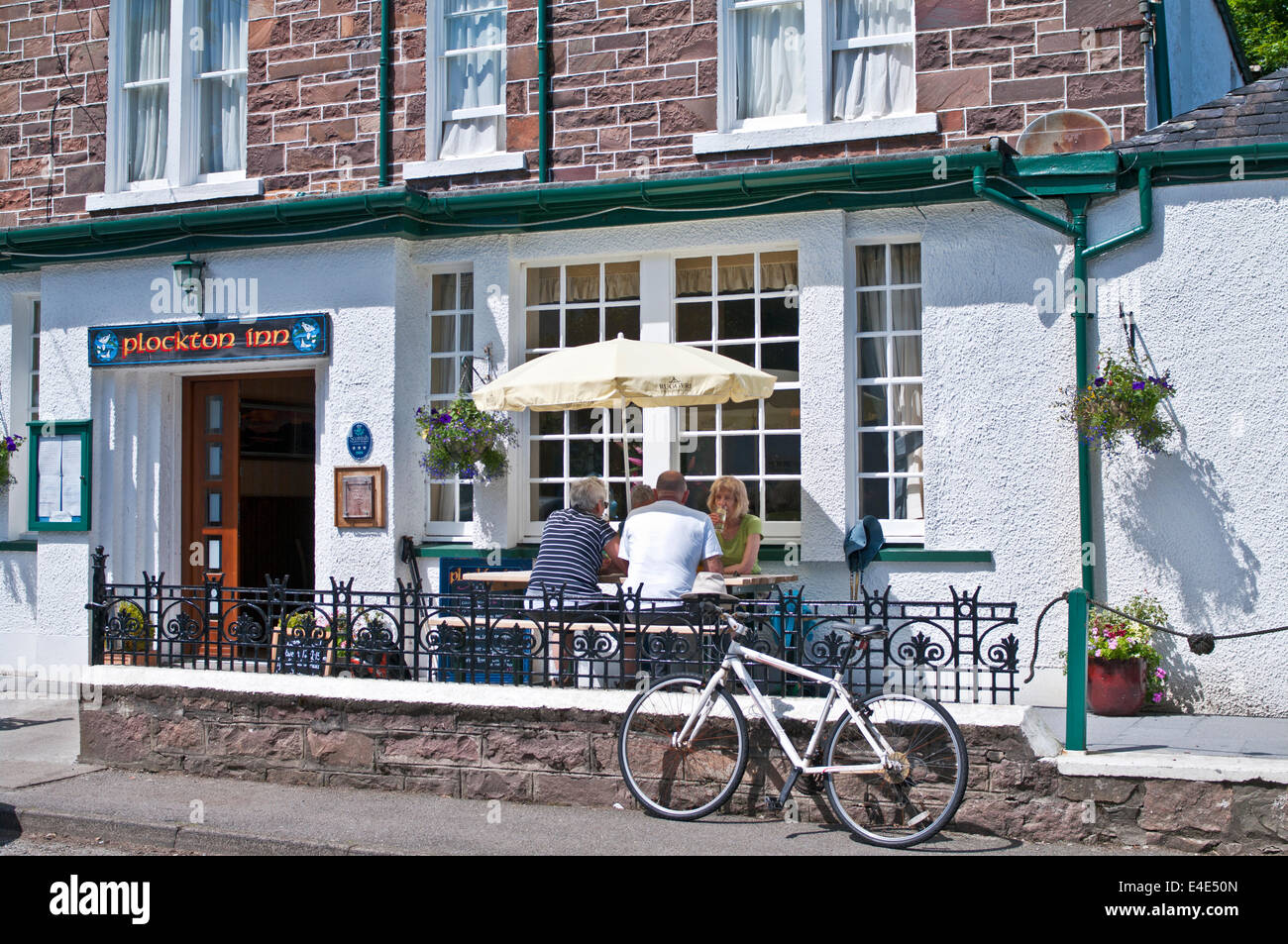 4 people sitting at lunchtime in summer sunshine on outside terrace at the Plockton Inn, renowned seafood restaurant, Plockton, Scottish Highlands Stock Photo