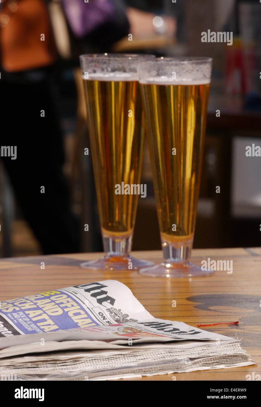 Two glasses of beer on a bar table with a newspaper and an out of focus background Stock Photo