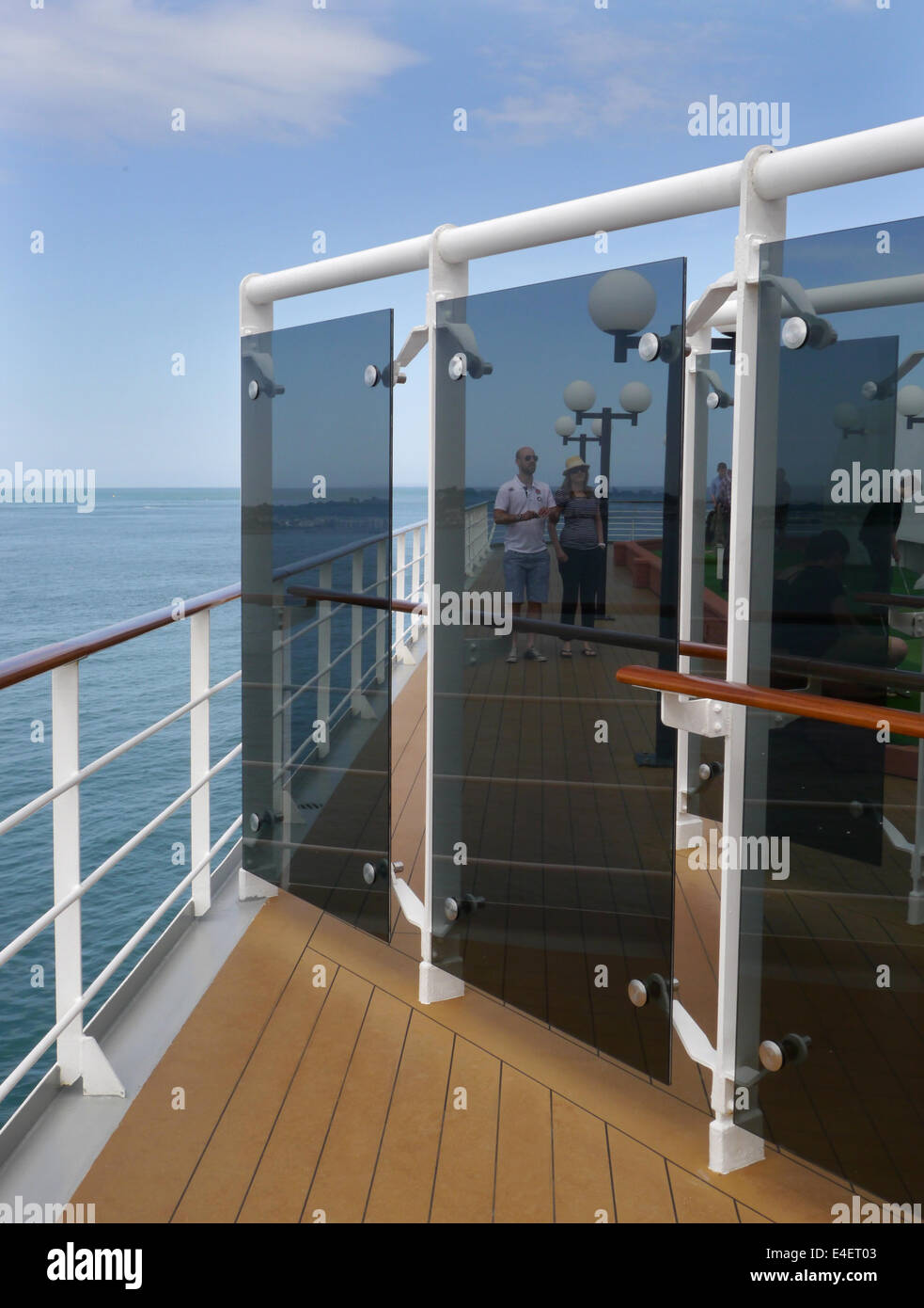 A Cruise Ship Deck With Glass Panels And People In The Distance
