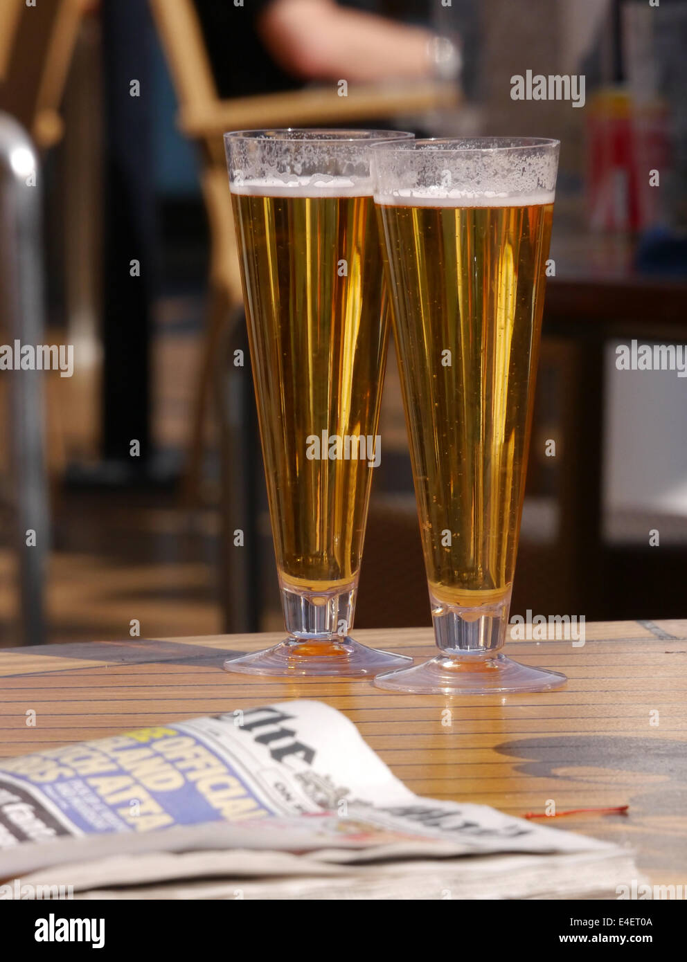 Two glasses of beer on a bar table with a newspaper and an out of focus background Stock Photo
