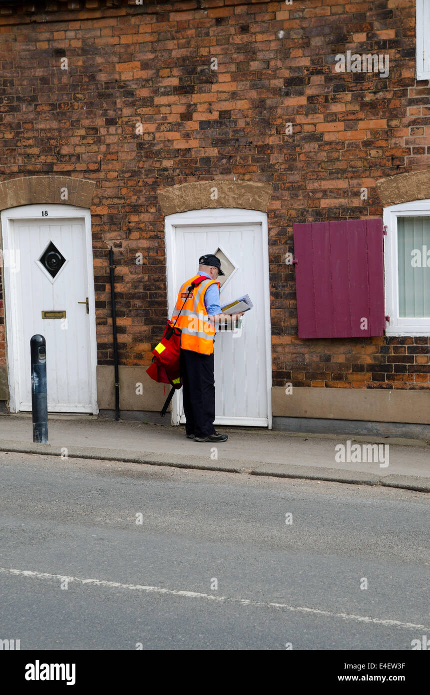 Postman posting letters at a terraced cottage Stock Photo