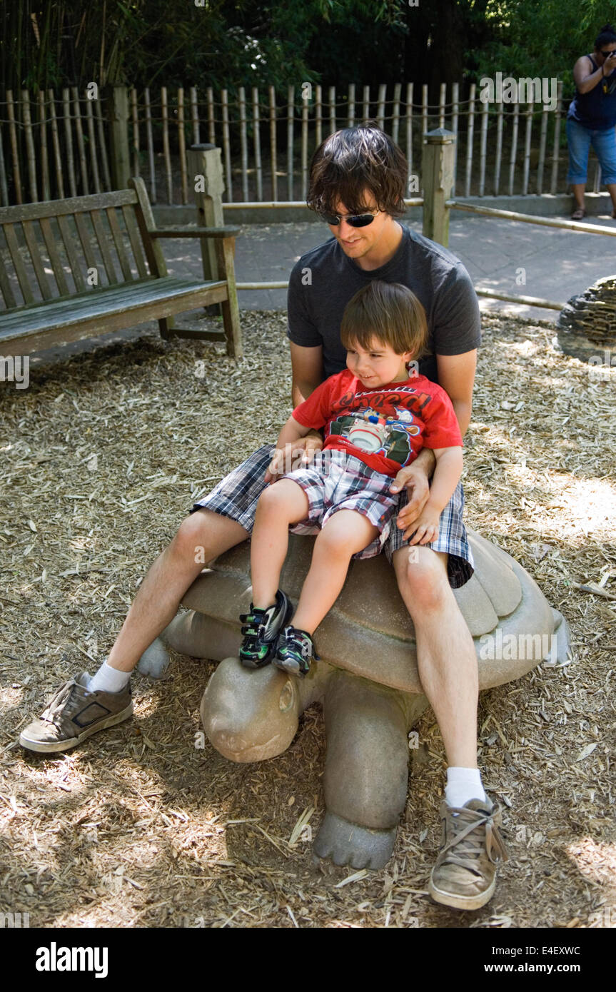 Young Father and Son Sitting on Stone Turtle at the Louisville Zoo in Kentucky Stock Photo