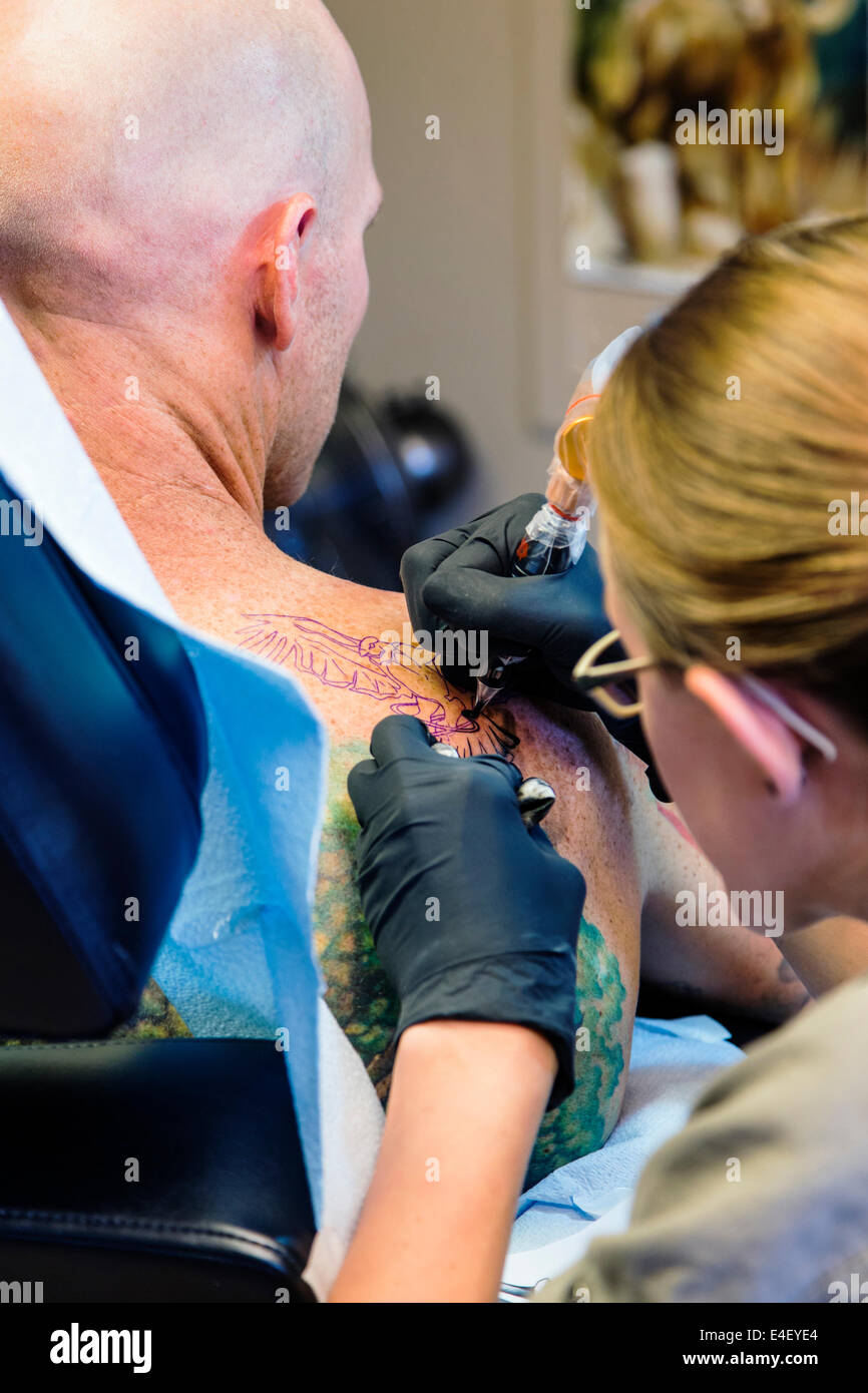 Woman tattooing an eagle on the back of a man Stock Photo