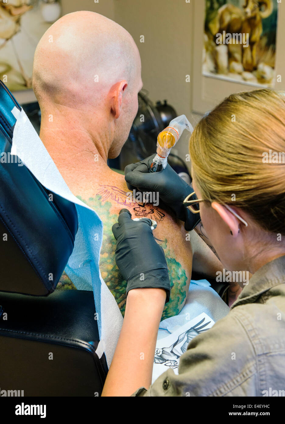 Woman tattooing an eagle on the back of a man Stock Photo