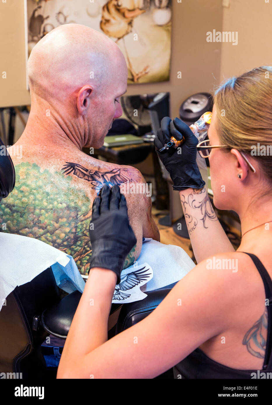Woman tattooing an eagle on the back of a man Stock Photo
