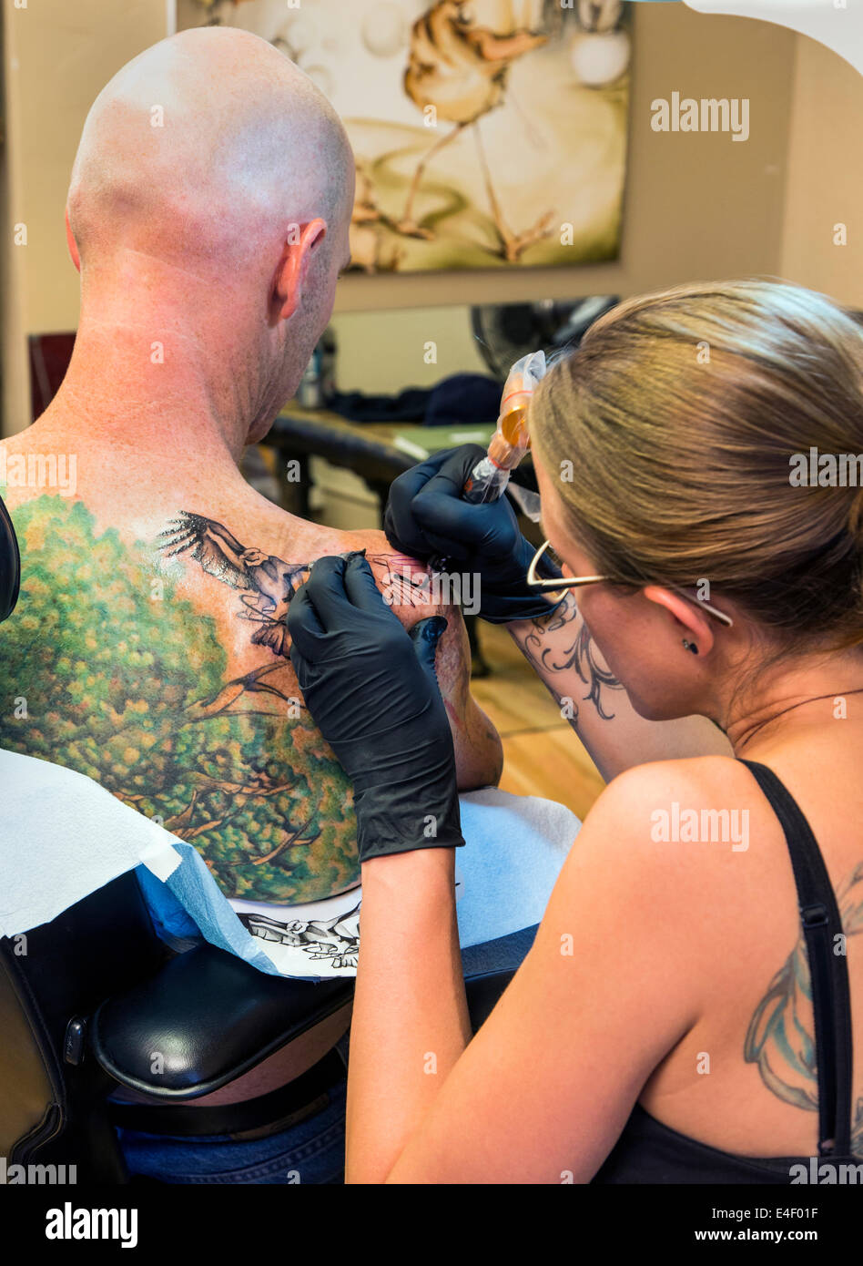 Woman tattooing an eagle on the back of a man Stock Photo