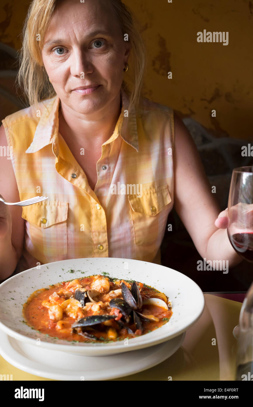 Mature Caucasian woman sitting at a table eating Caciucco, an Italian seafood soup with shrimp, mussels, and fish, and enjoying Stock Photo