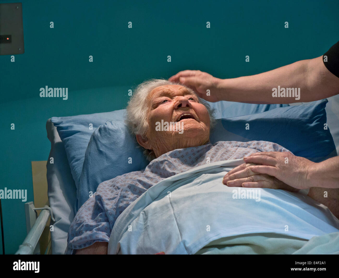 old age elderly lady in comfortable hospital care bed at night with comforting hand of carer nurse Stock Photo