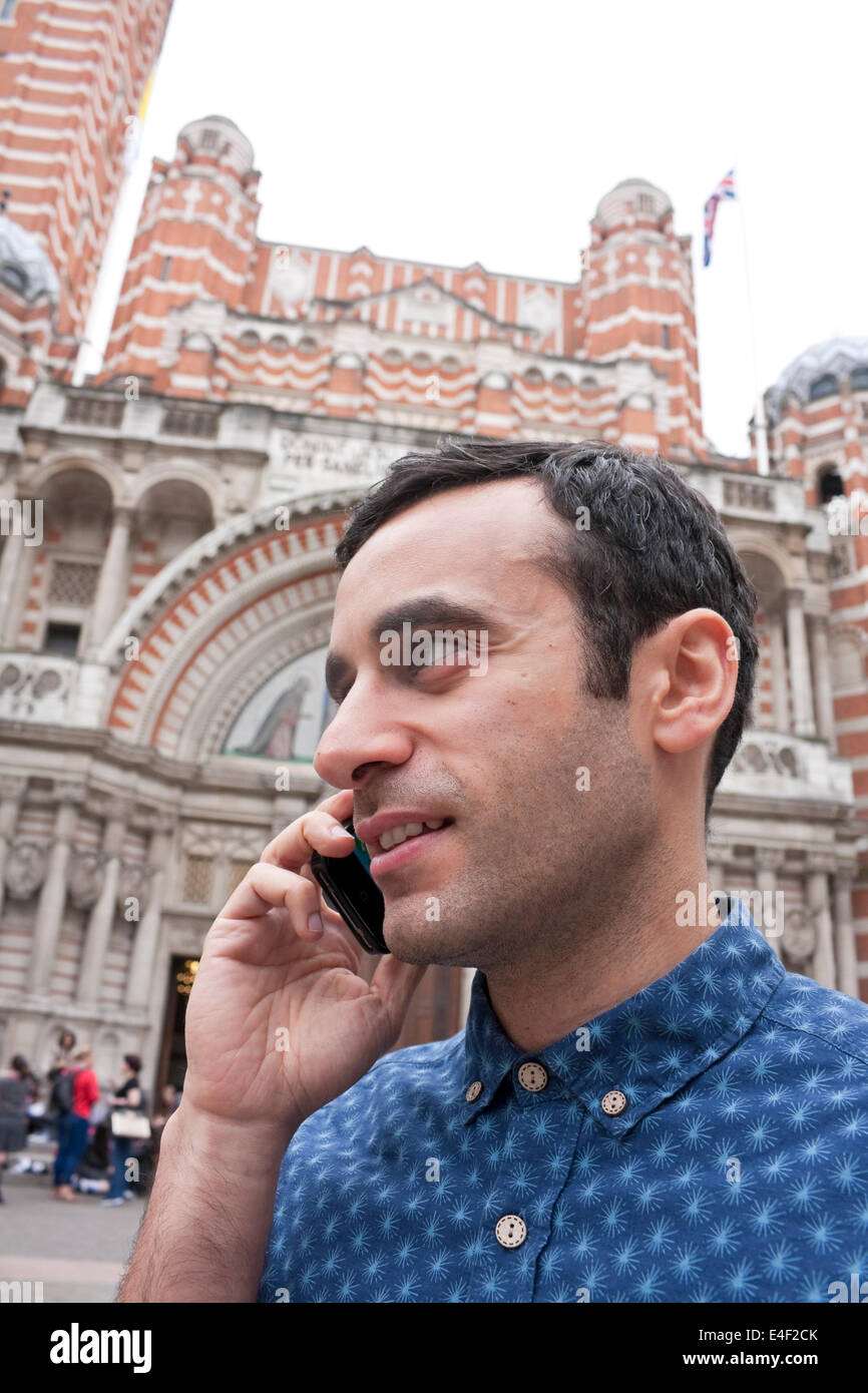 A mediterranean male talking on his smart phone with a church in background Stock Photo