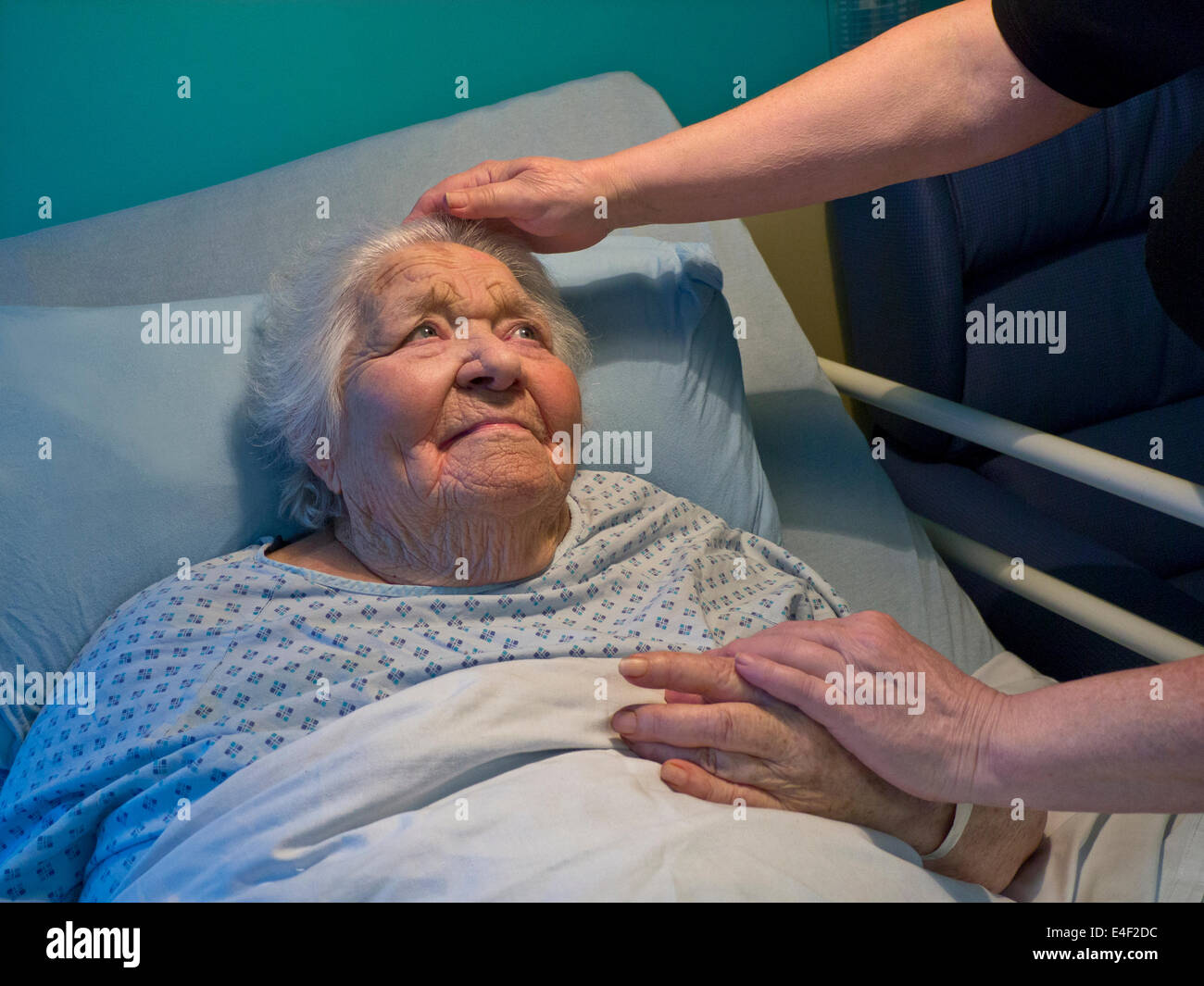 Senior lady old age elderly smiling content comfortable in hospital care home bed with comforting hand of carer nurse Stock Photo