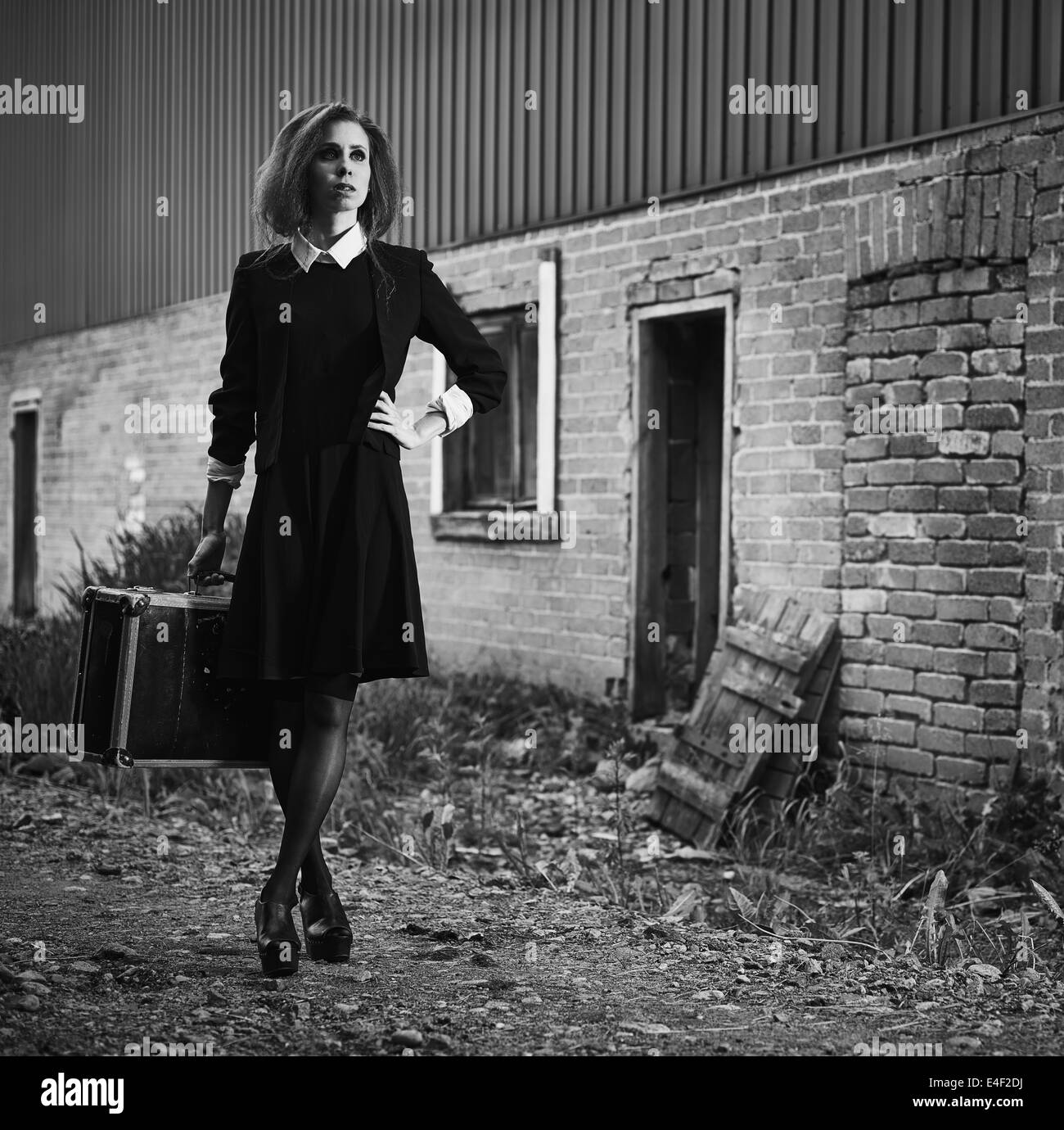 Fashionable young woman with her suitcase, old rural scene, black and white image Stock Photo