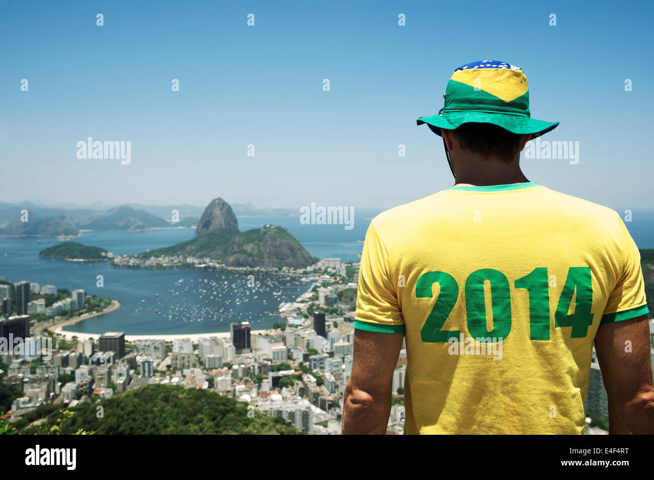 Man in Brazil hat and 2014 shirt standing at bright sunny Rio de Janeiro skyline with Sugarloaf Pao de Acucar Mountain Stock Photo