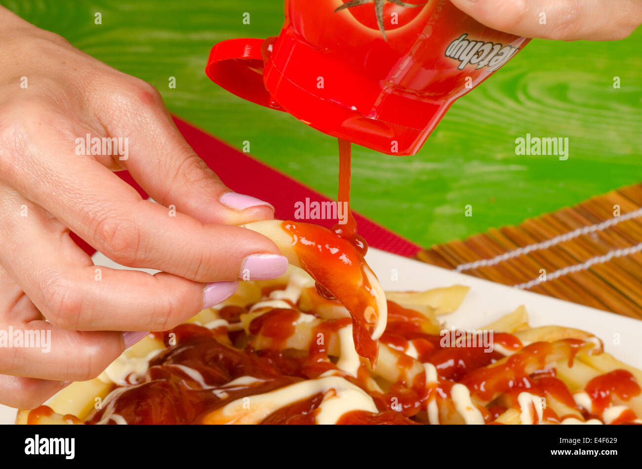 Hands pouring a huge amount of ketchup on a serving of French fries