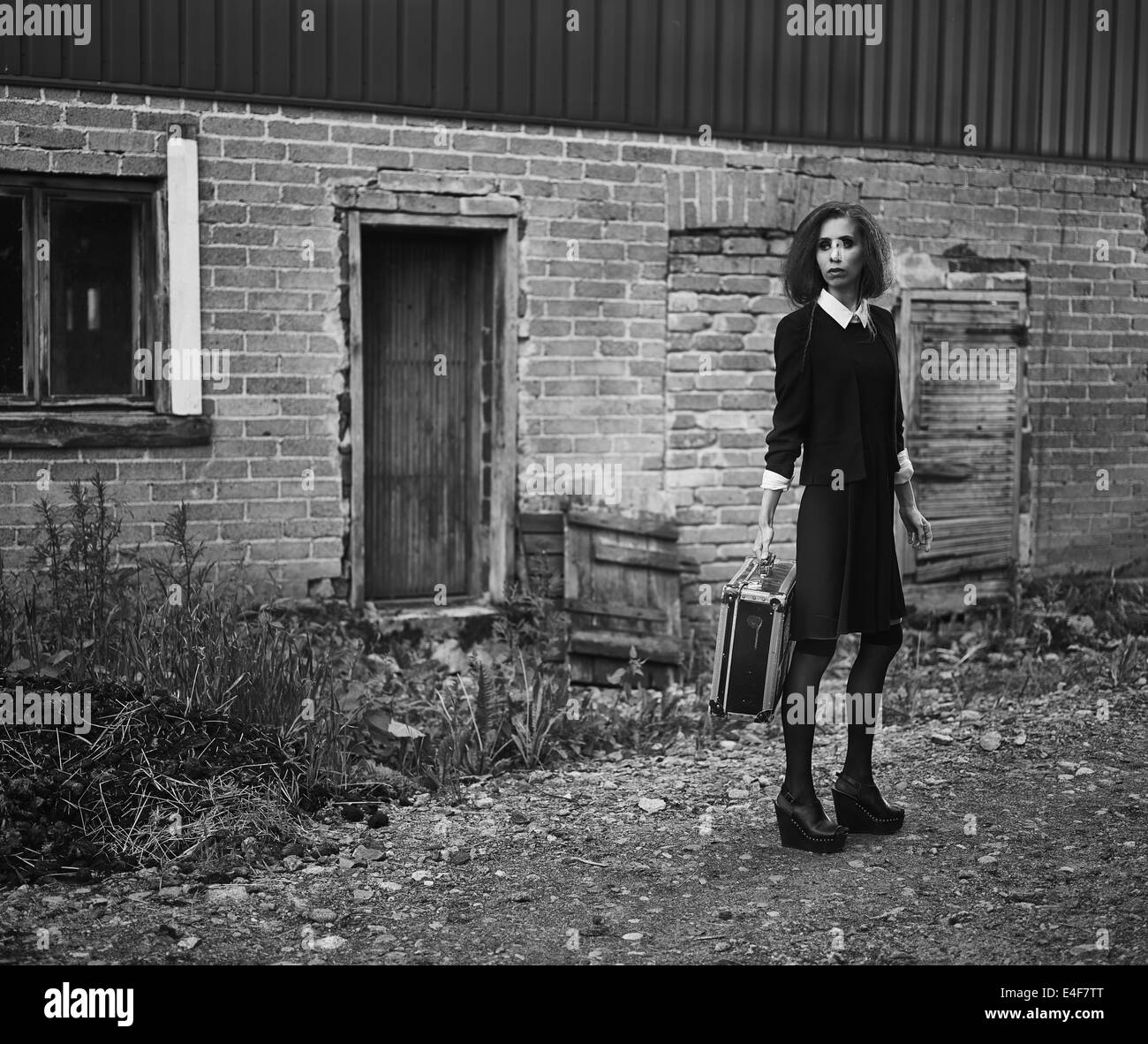 Fashionable young woman with her suitcase, old rural scene, black and white image Stock Photo