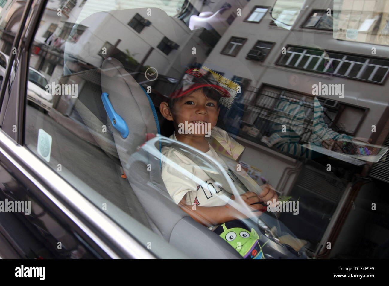 It's a photo of a young Eurasian Boy who sits in the back f a car in the babysit and wear the seatbelt Stock Photo