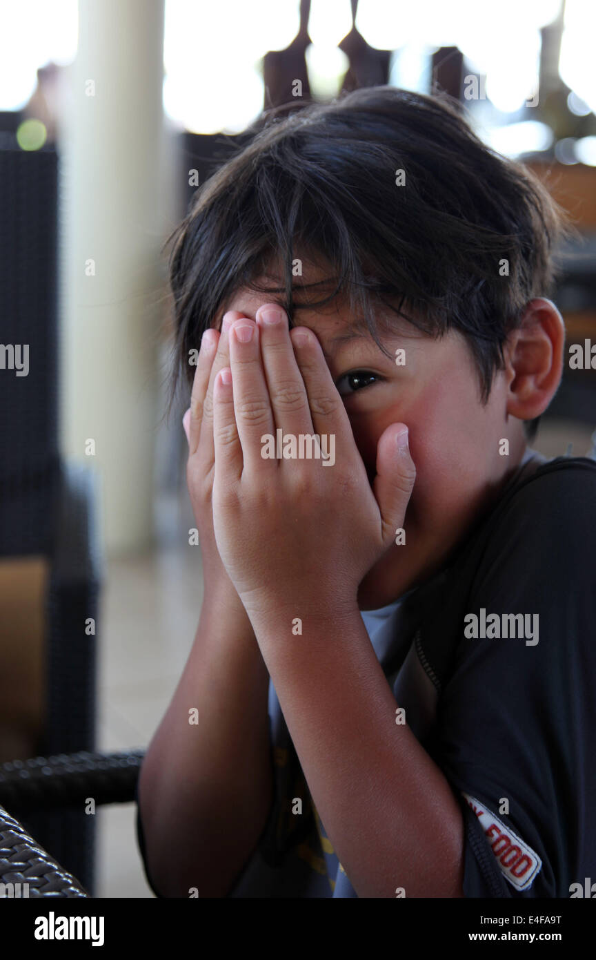 It's a photo of a young king who is hiding behind his hand as a playful boy. he is very happy of playing that Stock Photo