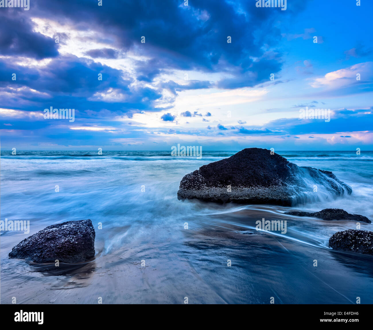 Tropical beach vacation background - waves and rocks on beach on sunset ...
