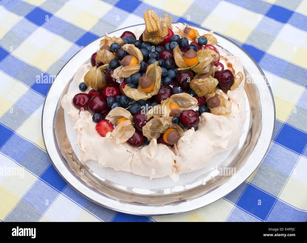 Fresh Fruit Pavlova, meringue topped with fresh fruit including physalis dipped in chocolate on a blue and white tablecloth Stock Photo