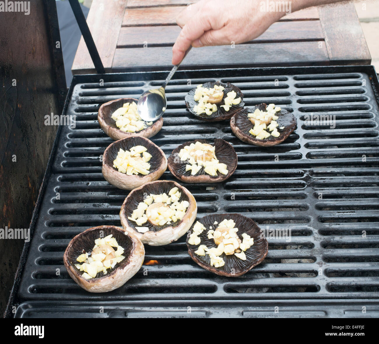 Man barbequeing large mushrooms with garlic using  a gas fired barbeque Stock Photo