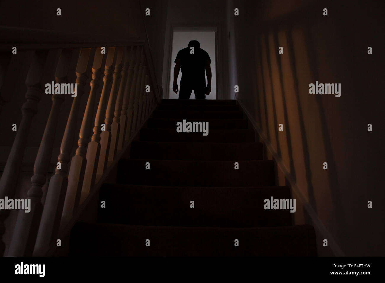 Silhouette of a man standing slumped at the top of a stairway, shadows cast on the walls from the light below. See similar shots Stock Photo