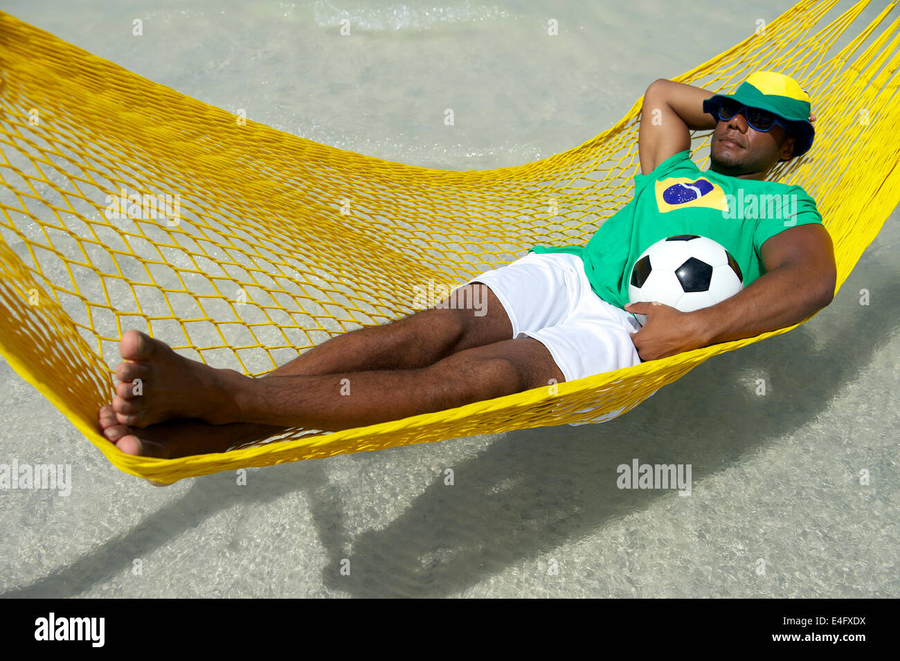 Brazilian football player wearing Brazilian flag hat relaxing in beach hammock with a soccer ball Stock Photo