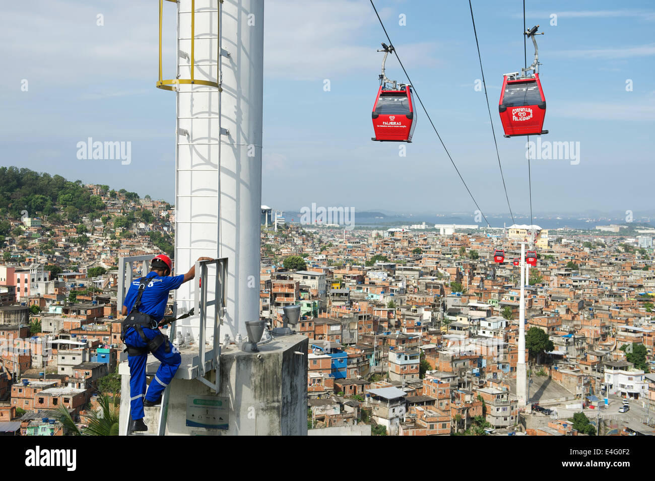 RIO DE JANEIRO, BRAZIL - OCTOBER 22, 2013: Maintenance worker climbs a post supporting cable cars above favela Complexo Alemao Stock Photo