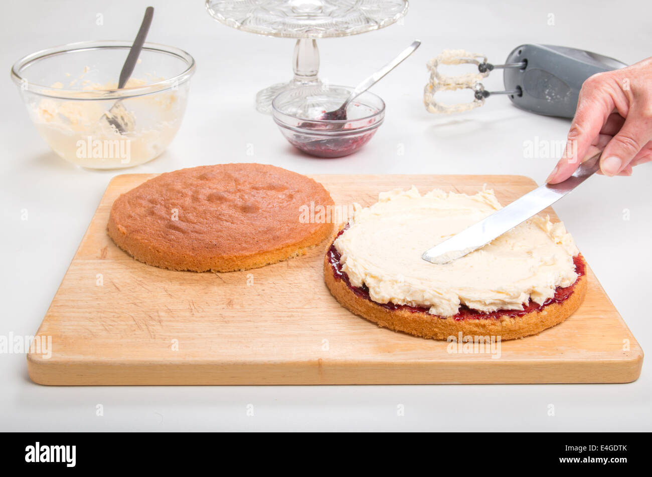 a victoria sponge cake sliced, jam spread, spreading butter cream with a palette knife [Land] 'making a cake'  (30 of 44) Stock Photo