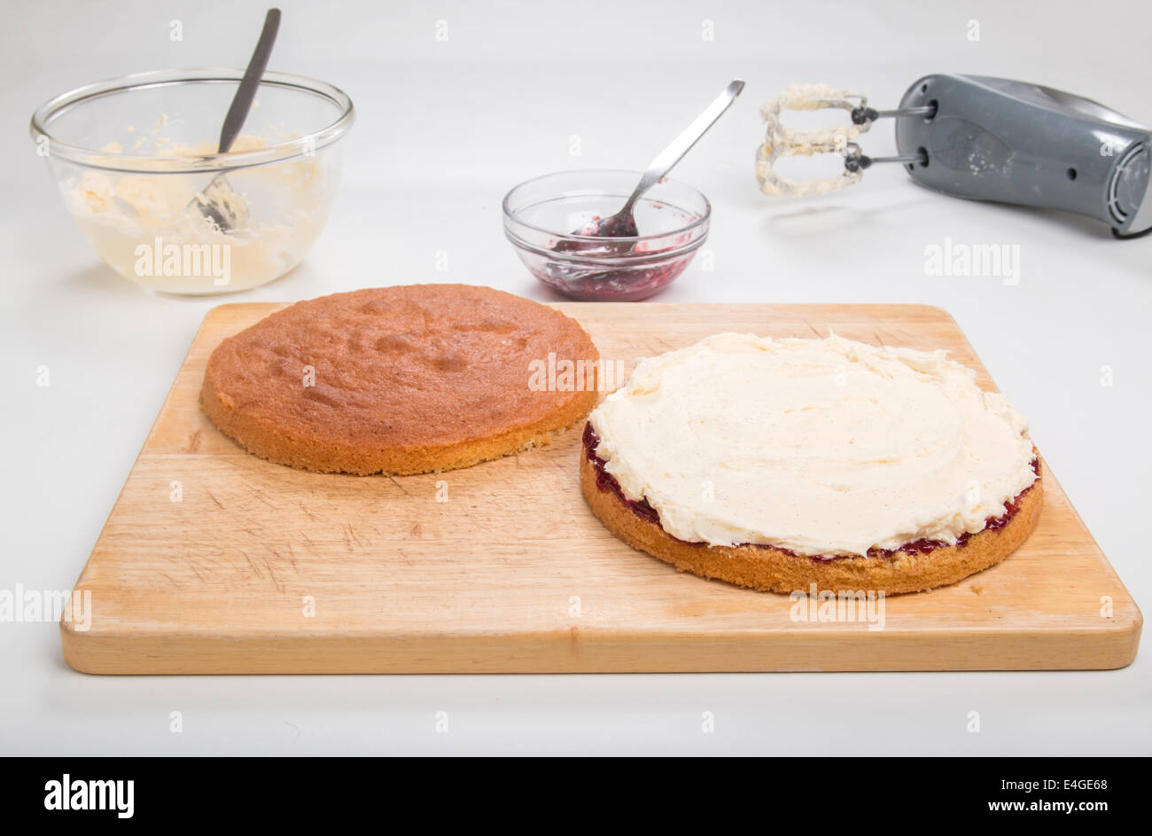 a victoria sponge cake sliced, jam spread, butter cream spread ready to put the top on  [Land] 'making a cake' (29 of 44) Stock Photo