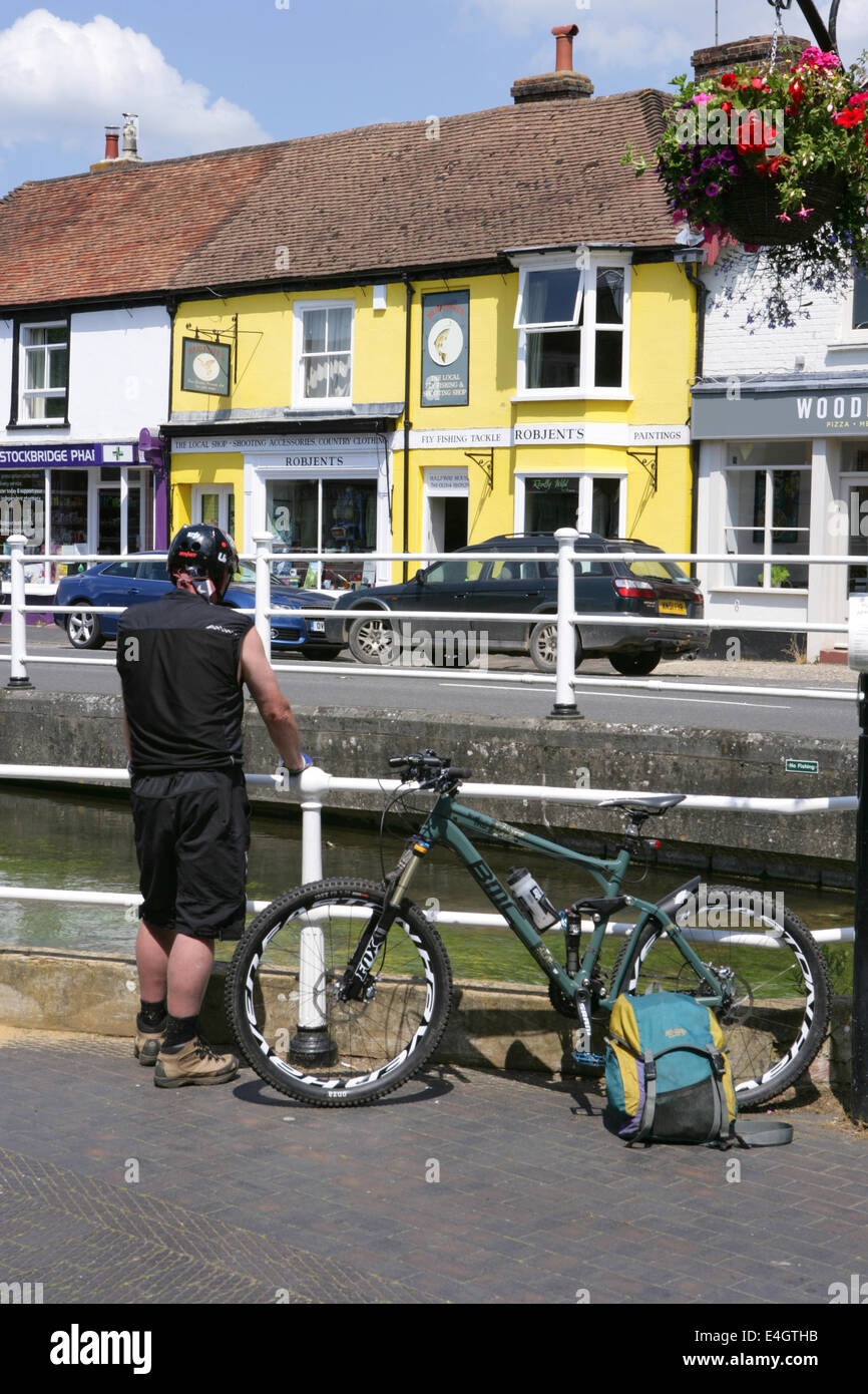 A cyclist takes a break beside the High Street in Stockbridge - a popular cycle route through Hampshire in the UK. Stock Photo